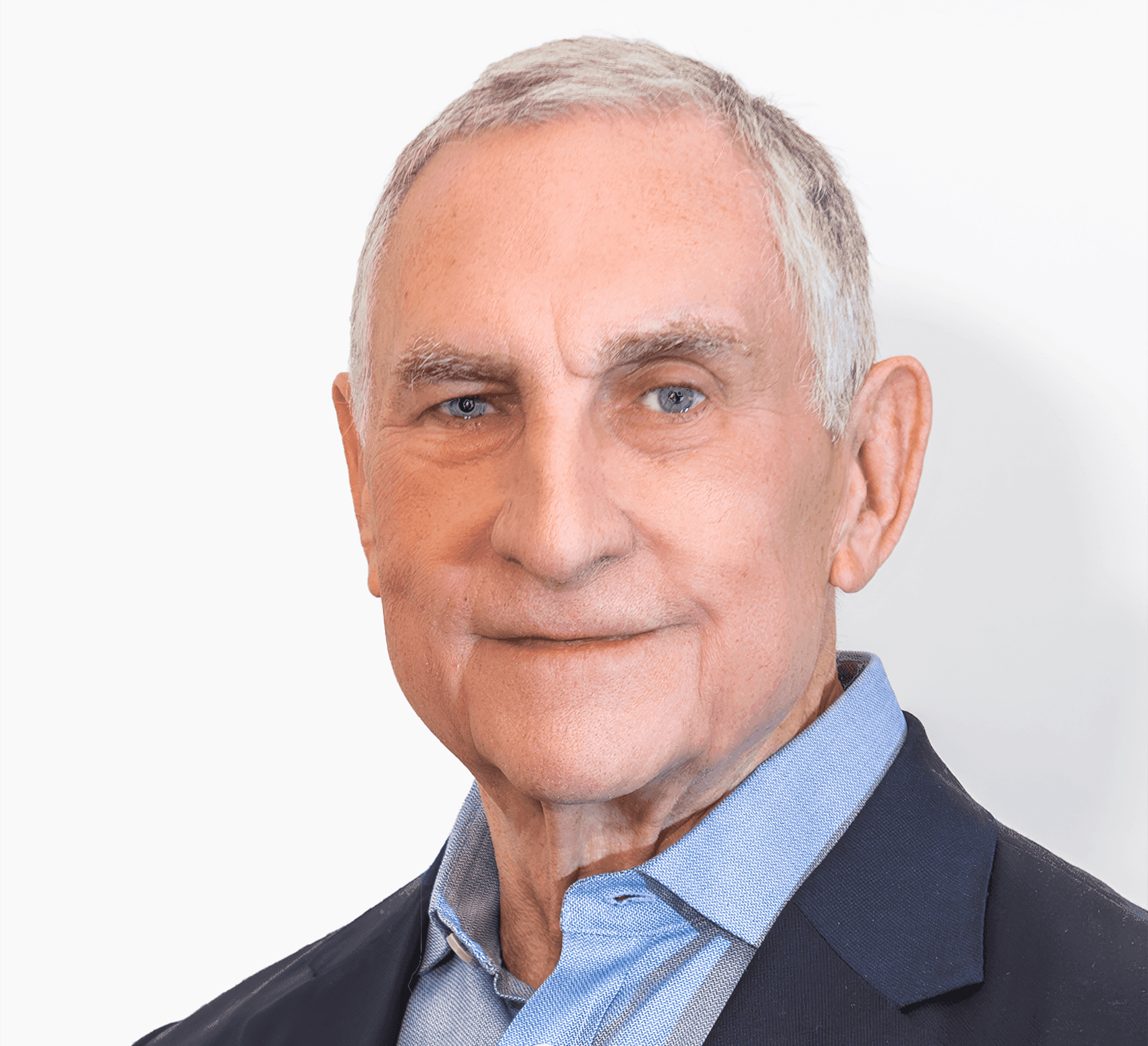 Headshot of John Hansen-Flaschen, a man with short gray-white hair and blue eyes. He wears a light blue button-down shirt under a navy blazer, and stands against a plain white wall.