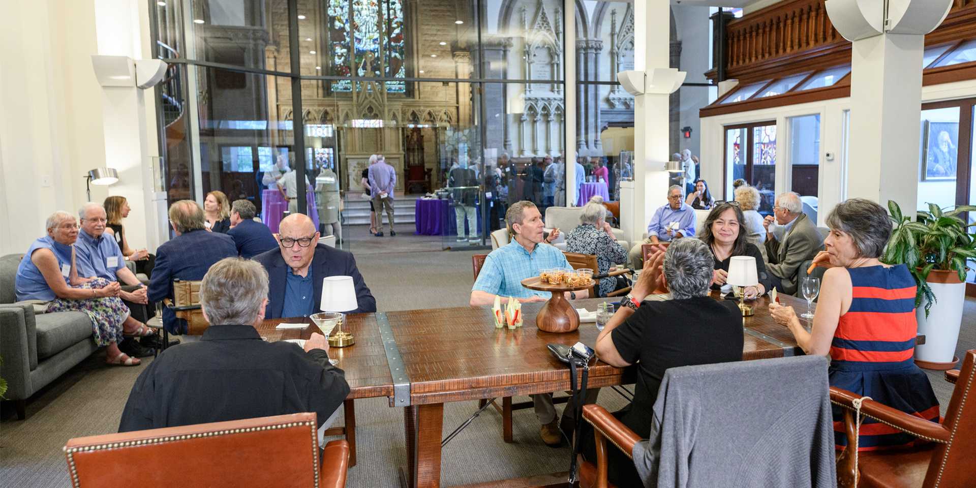 Photo of Fellows seated in a large room with tables and chairs, couches, and side offices
