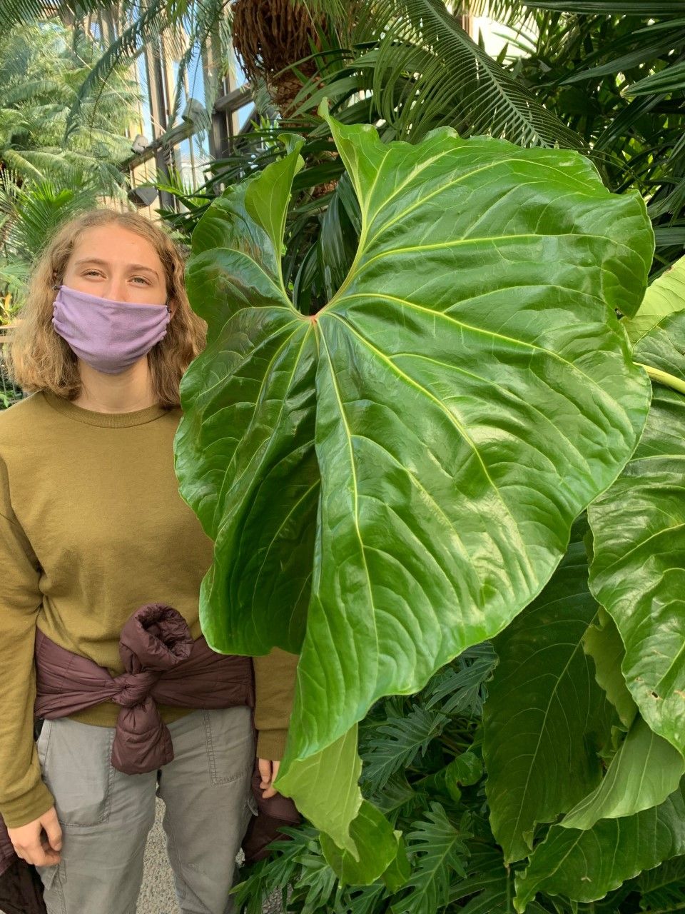 A blonde-haired White woman with a purple facemark stands next to a large leaf