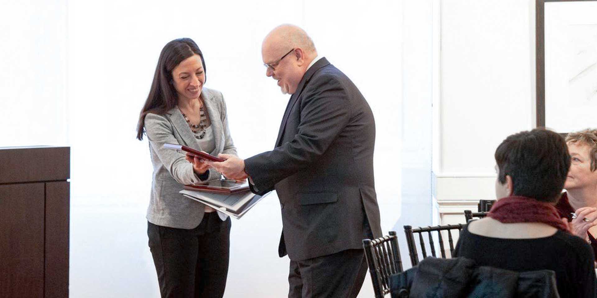 Man in suit accepting award from a woman in a gray blazer