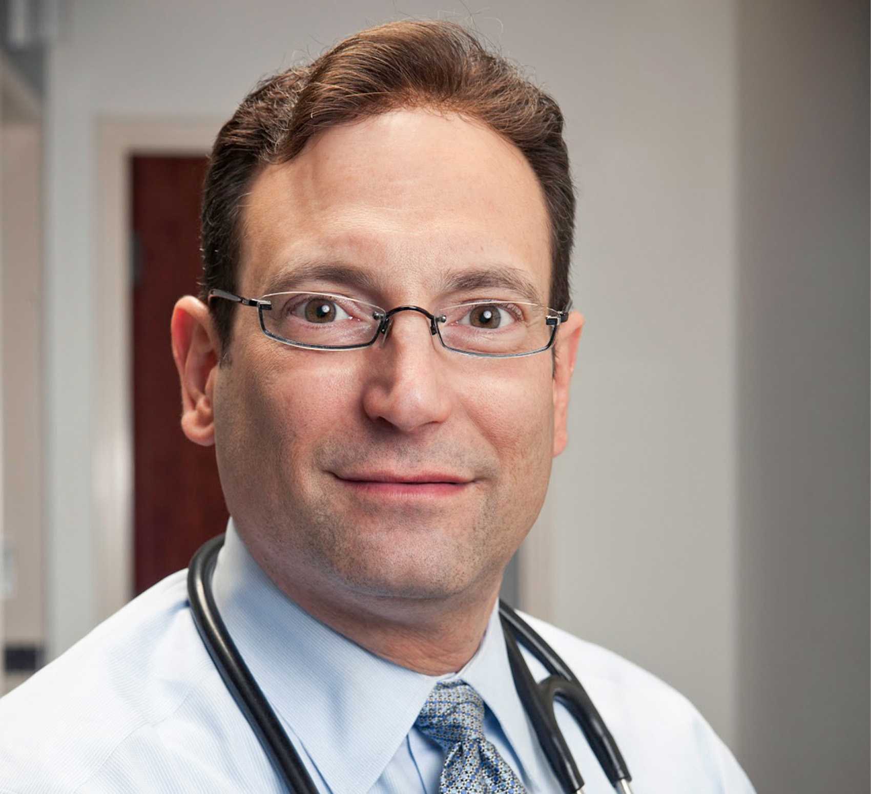 Headshot of Dr. Cirigliano. A man with short brown hair and dark, oval glasses faces the camera, in a white coat with a stethoscope draped around his neck 