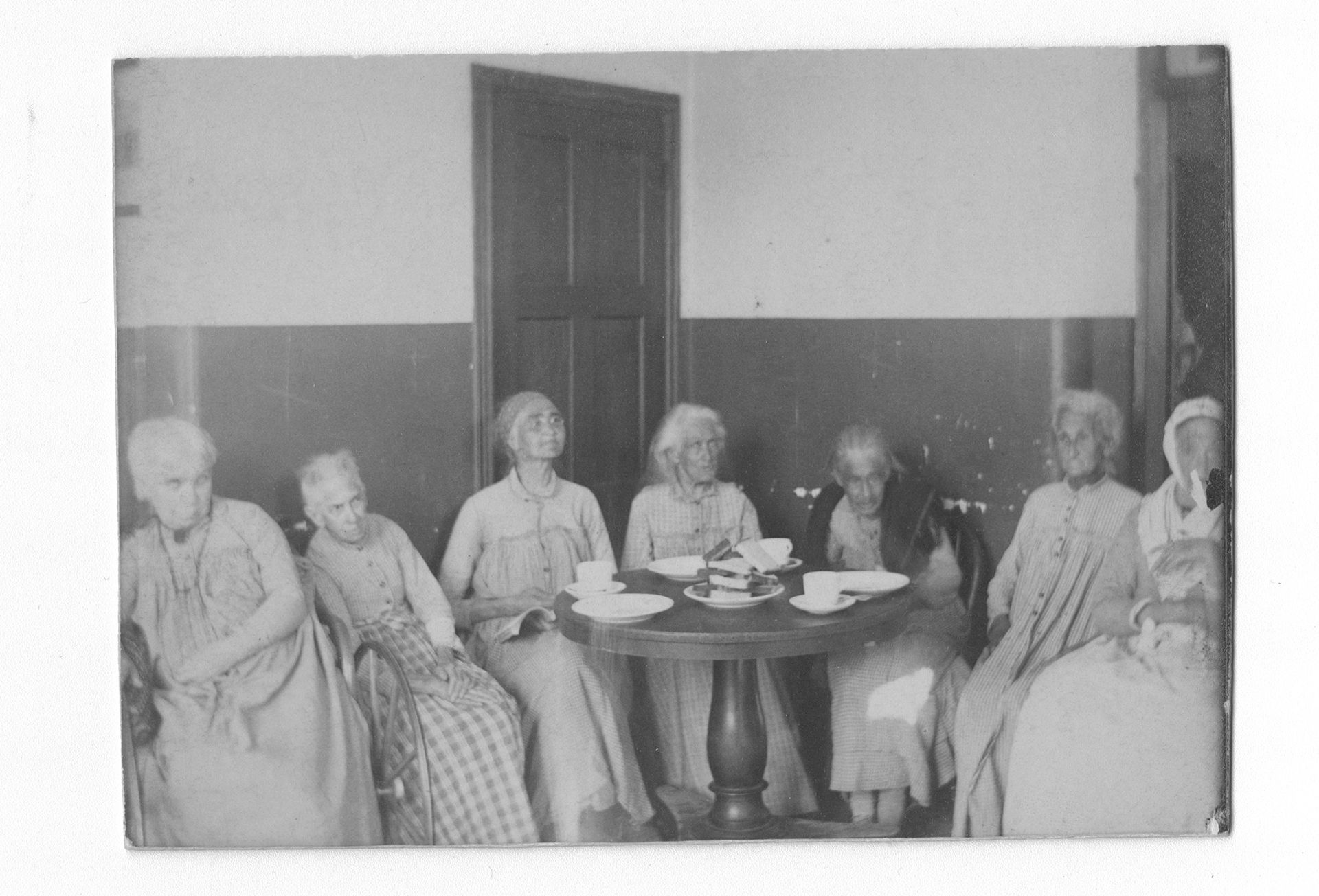 Seven female patients in the &quot;Insane Department&quot; at Philadelphia General Hospital sit around a small table.