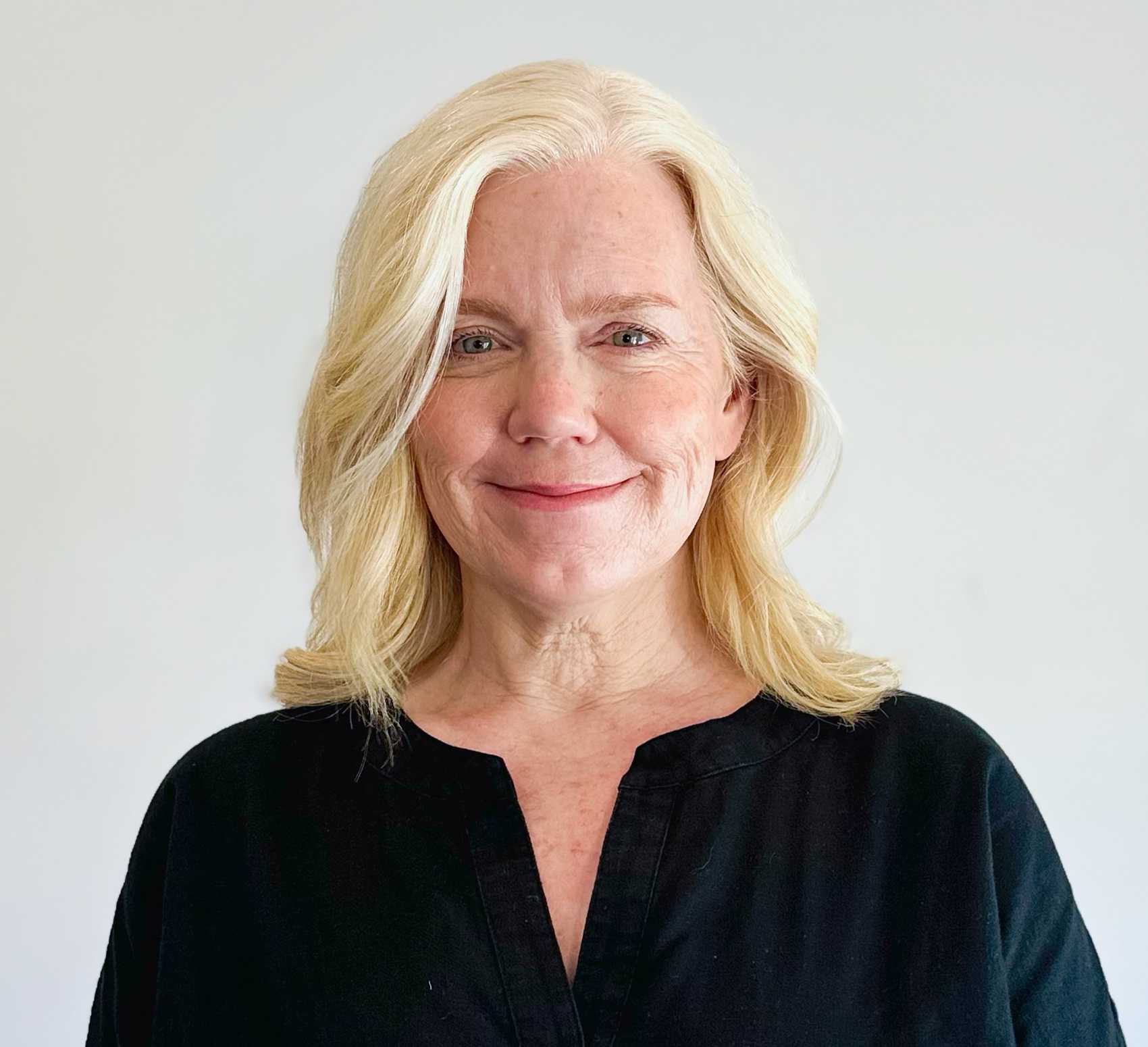 Headshot of a woman with light blonde, shoulder-length hair and a black top against a white background