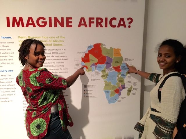 Binta and Adunia, two students from the Teva Pharmaceuticals Internship Program, pose in front of the main label for the Penn Museum's "Imagine Africa" exhibit
