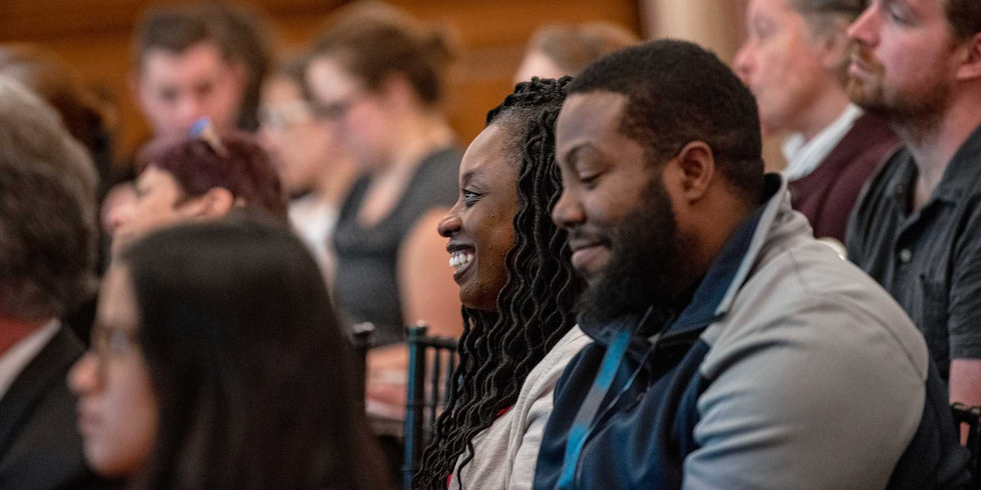 Two smiling people in a lecture crowd