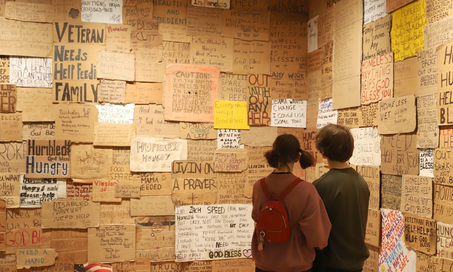 Two people looking at a wall of cardboard signs.