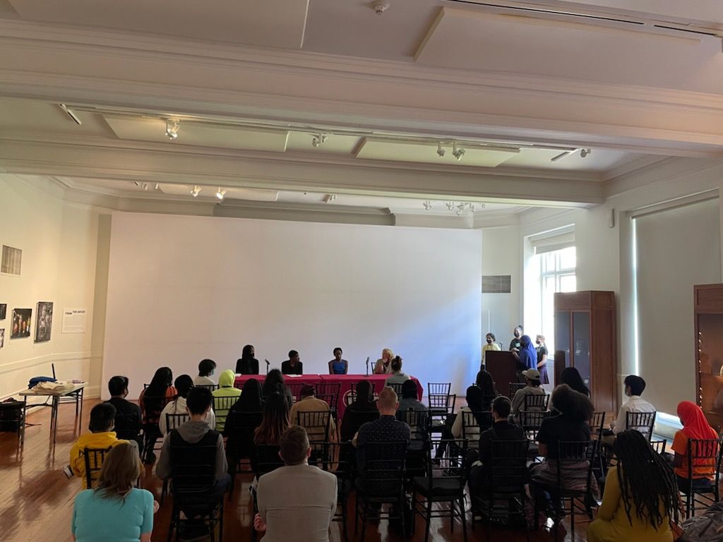 Four people seated at a table in front of a group of people in an auditorium.
