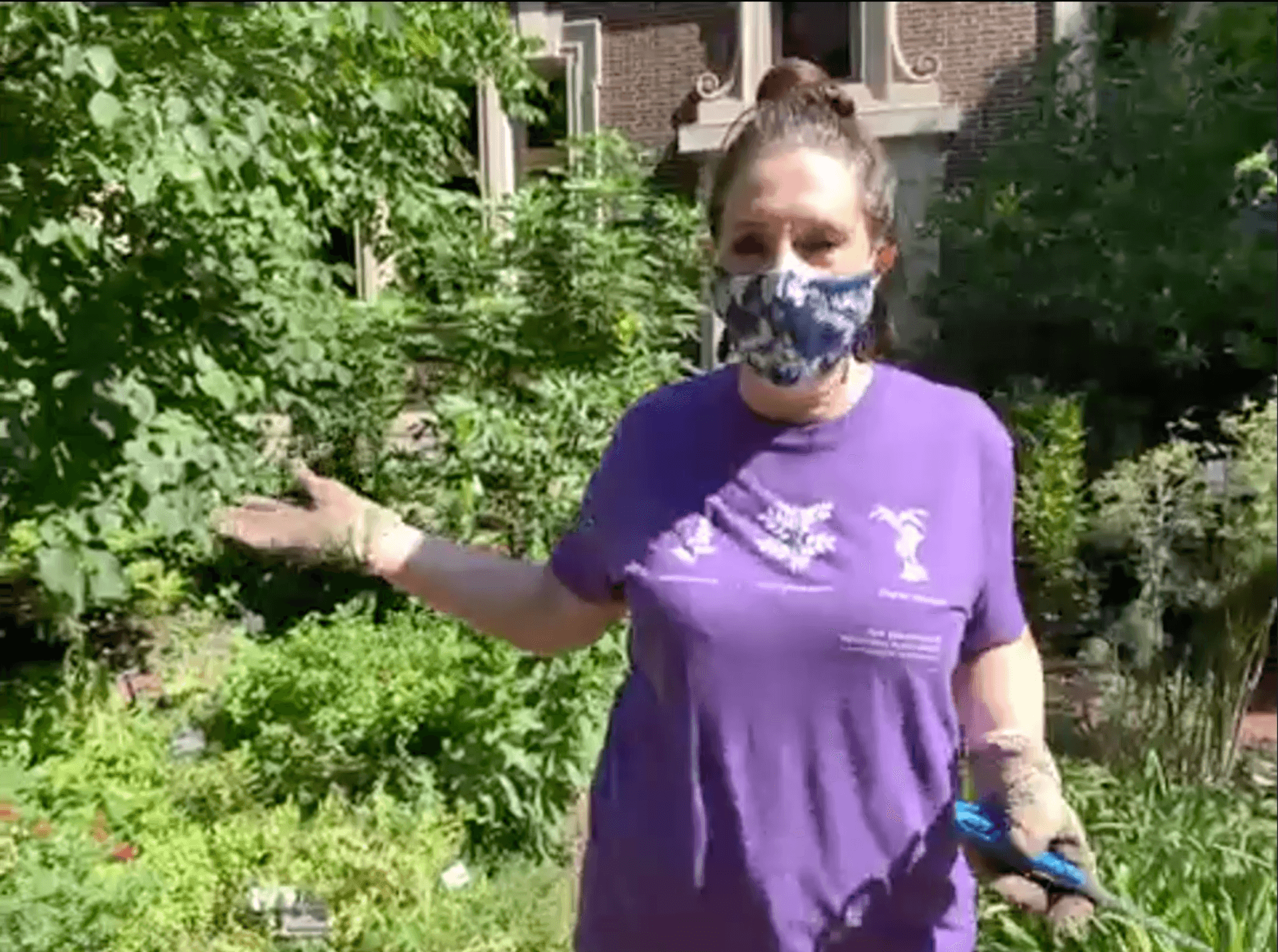 Jacqui Bowman, co-director of living exhibits, in a mask gestures to a plant in the Rush Garden