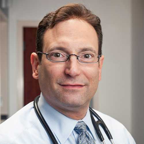 Headshot of Dr. Cirigliano. A man with short brown hair and dark, oval glasses faces the camera, in a white coat with a stethoscope draped around his neck 