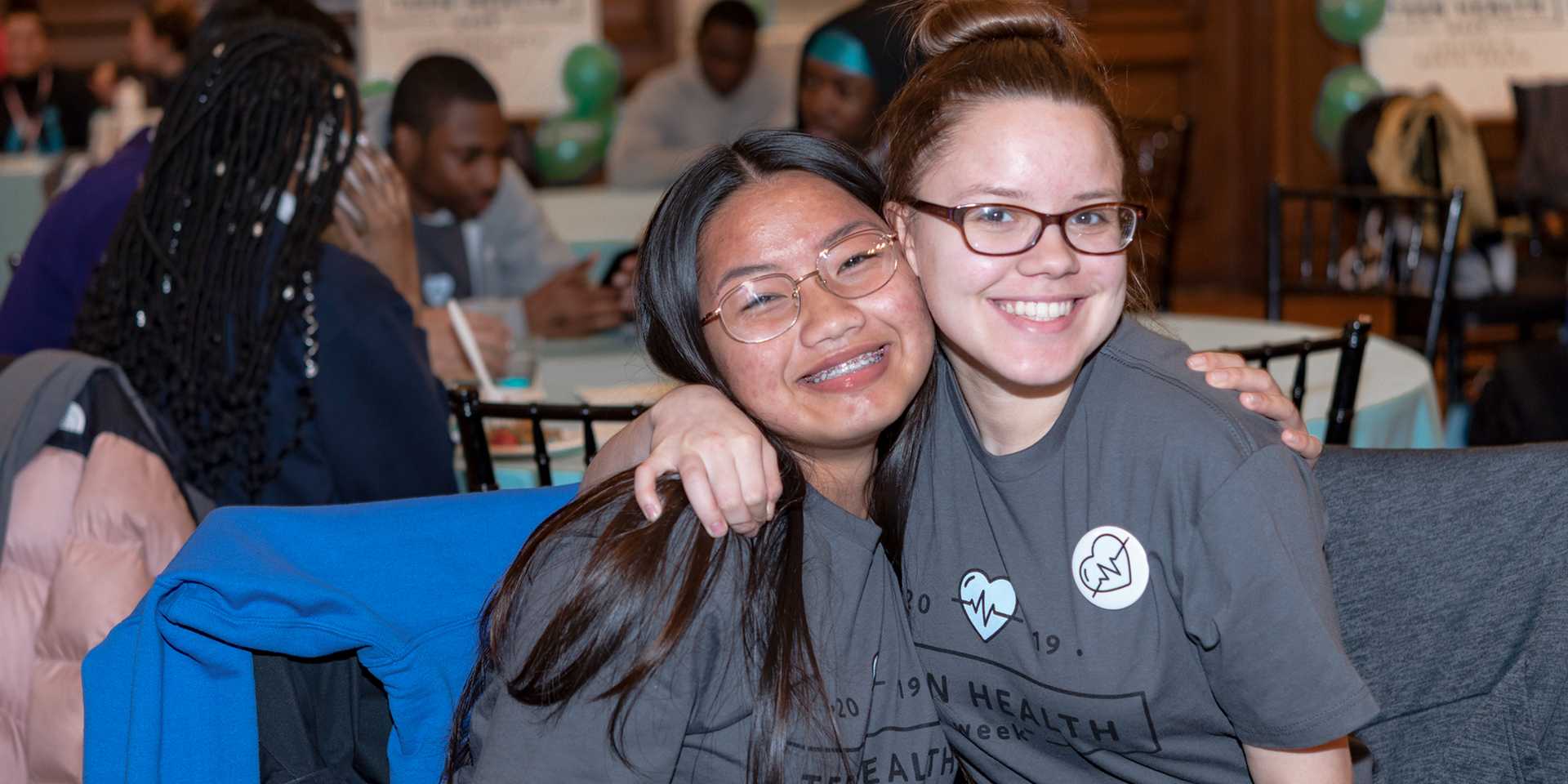 Two teen girls in gray shirts hugging and smiling