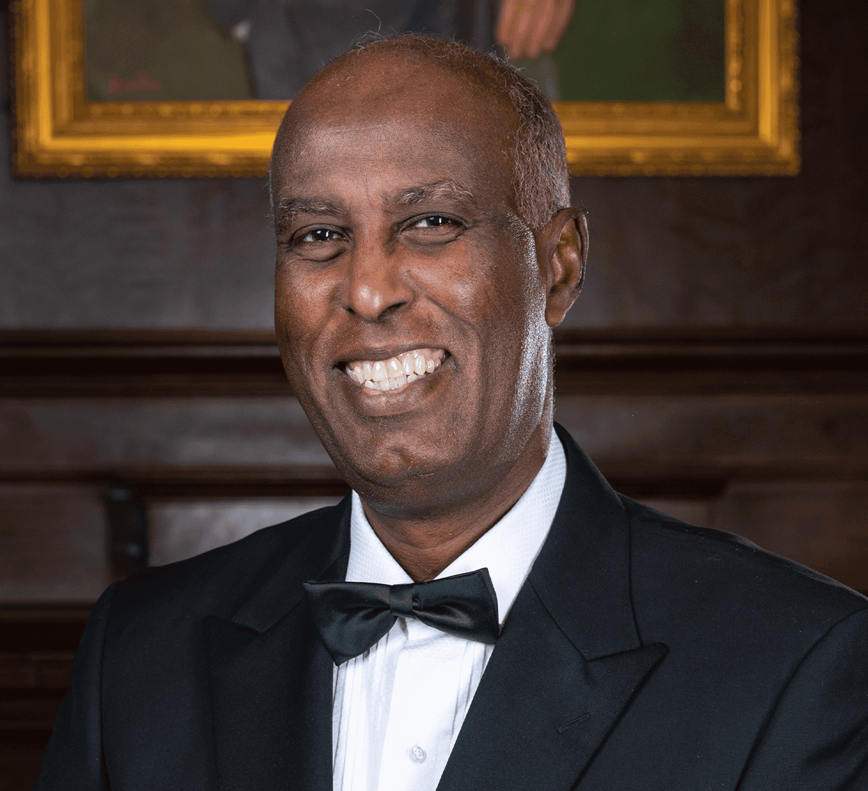 Headshot of Dr. Ibrahim standing in a black tuxedo with a bowtie against a wood paneled wall 