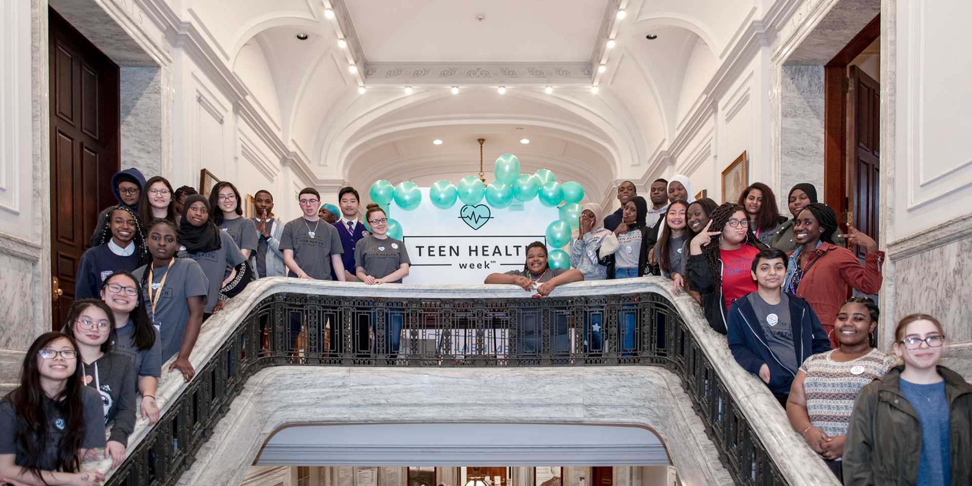 Group of teens standing around a poster that says "Teen Health Week"