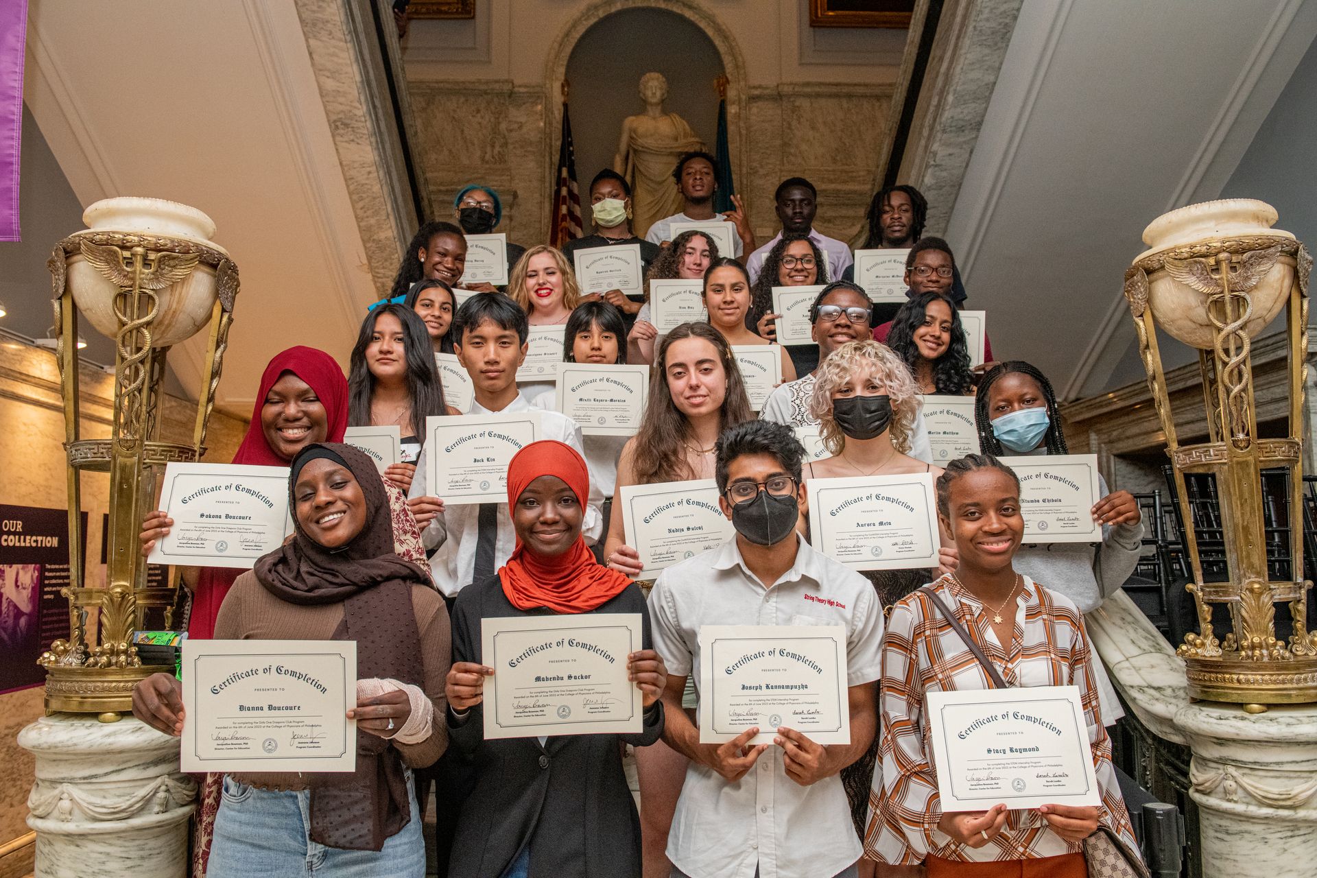 High school students stand together holding diplomas.